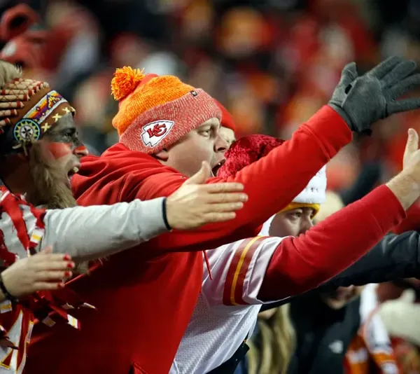 Fans of the Kansas City Chiefs football team in the stands making chopping motions with their hands.